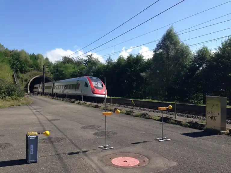 A SBB's ICN is coming out of a tunnel. Beside the track, yellow measurement equipment is visible