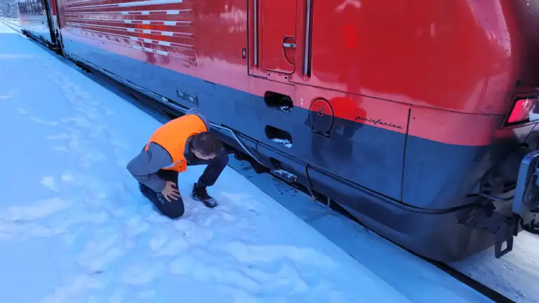 Ein Enotrac Mitarbeiter mit Leuchtweste schaut unter eine Re460 in Schneelandschaft
