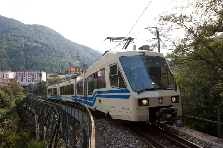 Alter FART-Triebzug auf einer Stahlbrücke vor einem Tessiner Dorf