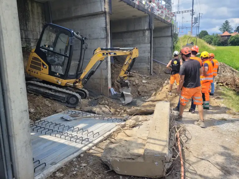Tiefbauarbeiten an einer Bahnlinie. Zu sehen ist ein kleiner Bagger und fünf Arbeiter