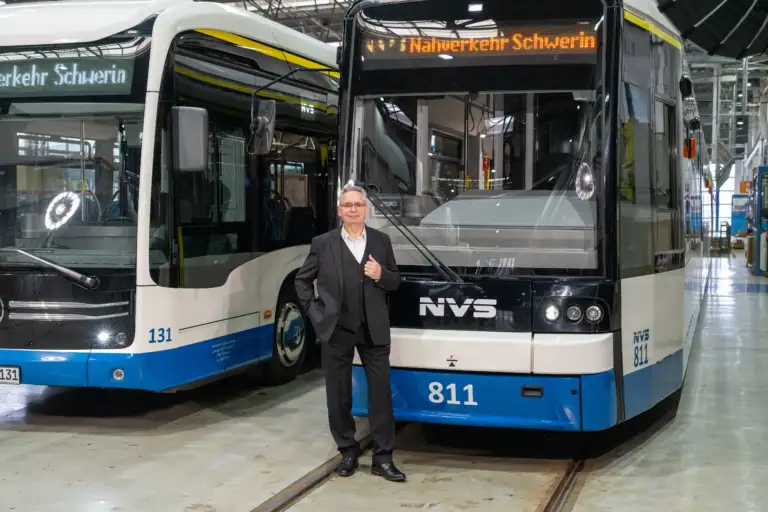 Portrait von Lothar Matzkeit, der in Anzug vor einem Tram und einem Bus posiert.