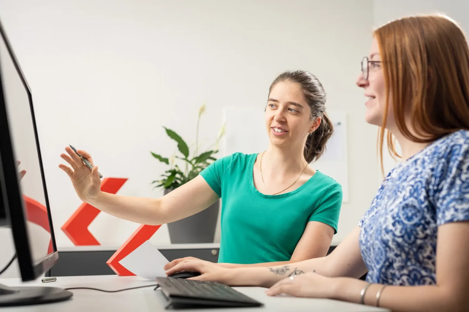 Enotrac Mitarbeiterinnen am Schreibtisch. Sie diskutieren über Sponsoring.