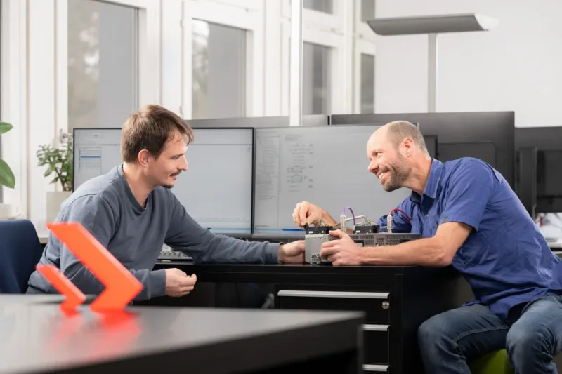 Teamwork bei Enotrac. Ein erfahrener Enotrac Mitarbeiter zeigt einem jüngeren Mitarbeiter etwas.